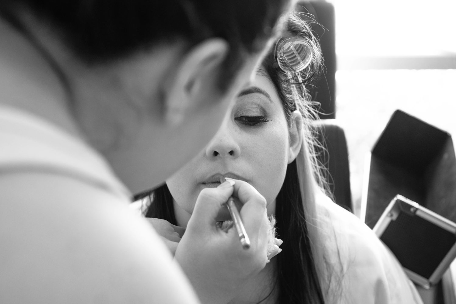 Black and white photo of bride getting makeup done. Lipliner being applied. Long eyelashes. Getting ready for wedding MUA
