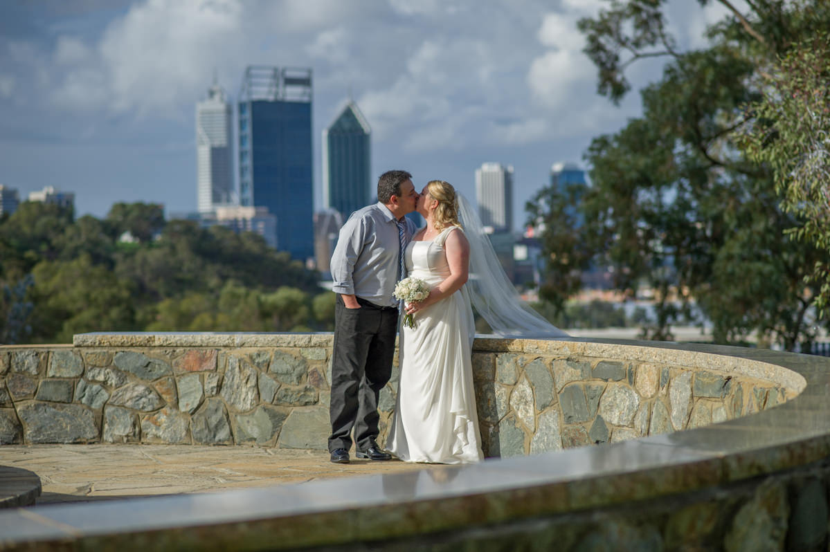 Bride and groom kissing at King's park with Perth city buildings
