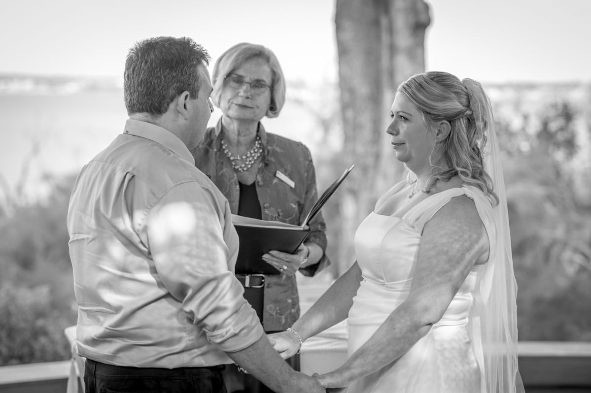 Black and white photo of bride and groom holding hands saying their vows