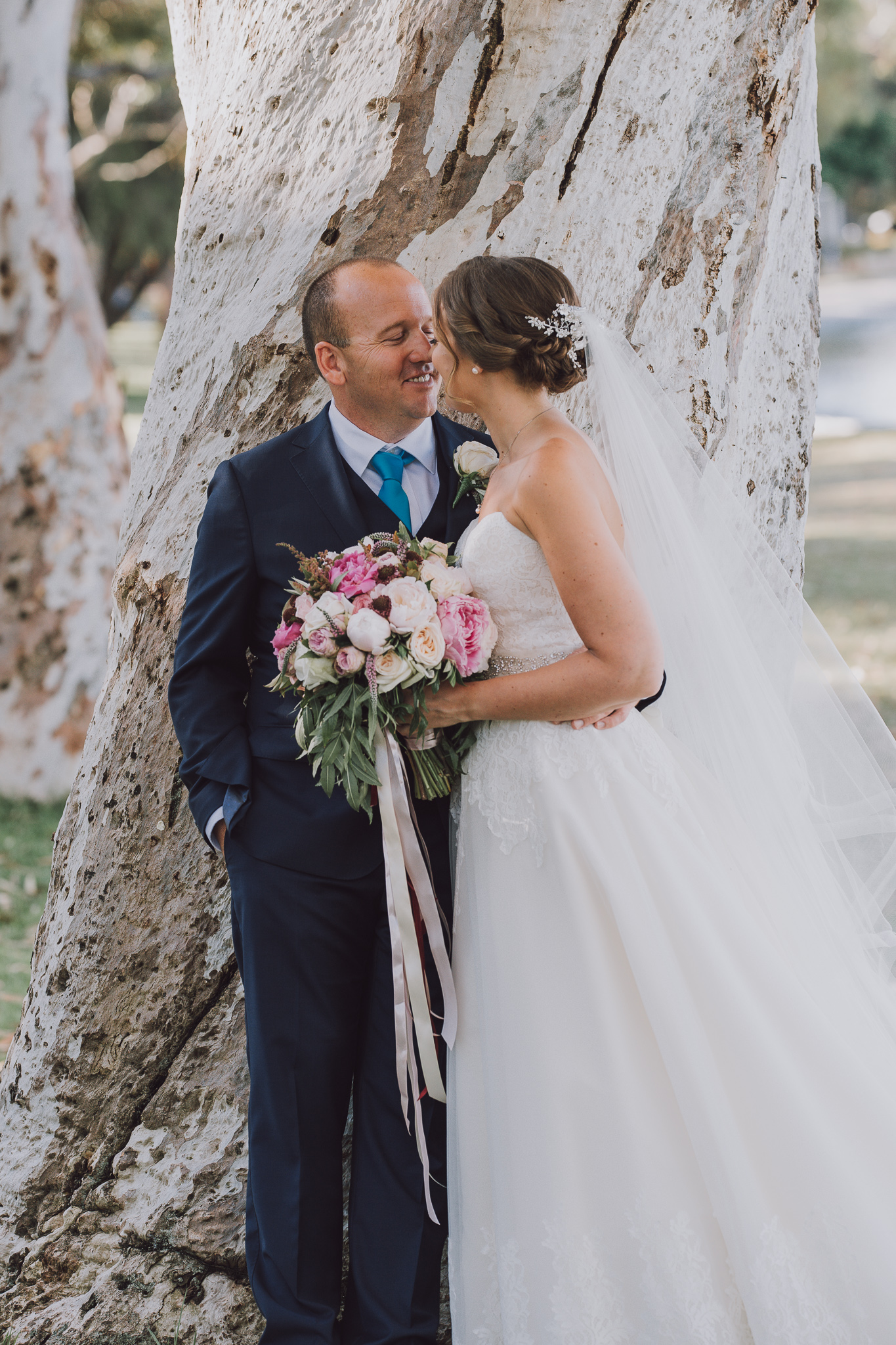 groom smiling at the bride next to tree