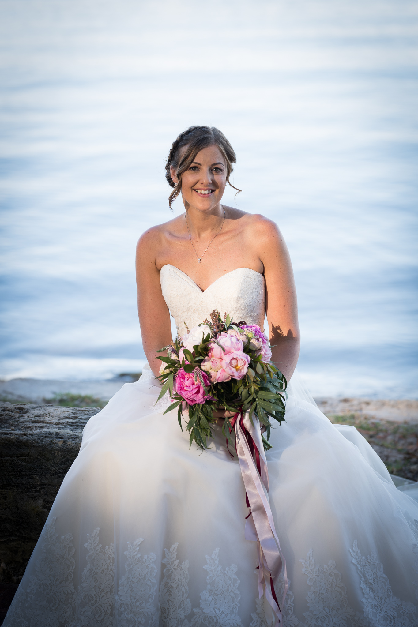 portrait of bride sitting down with water behind her